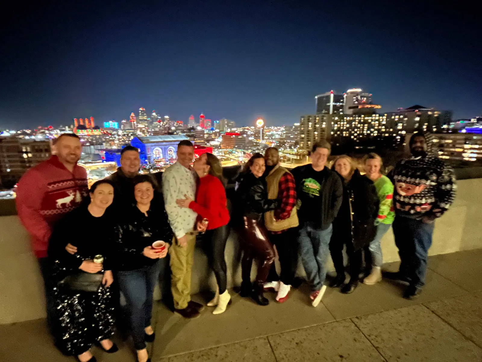 A holiday tour group at the Liberty Memorial overlook with the lit Kansas City skyline behind them